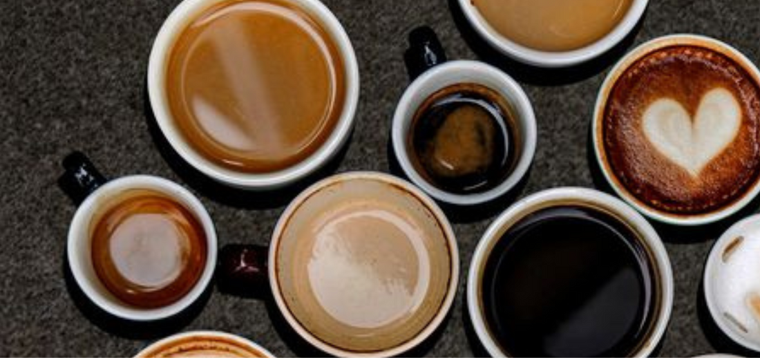 Overhead view of coffee cups in a semi-circle on a dark background, featuring various coffee styles. Minimalist and warm.